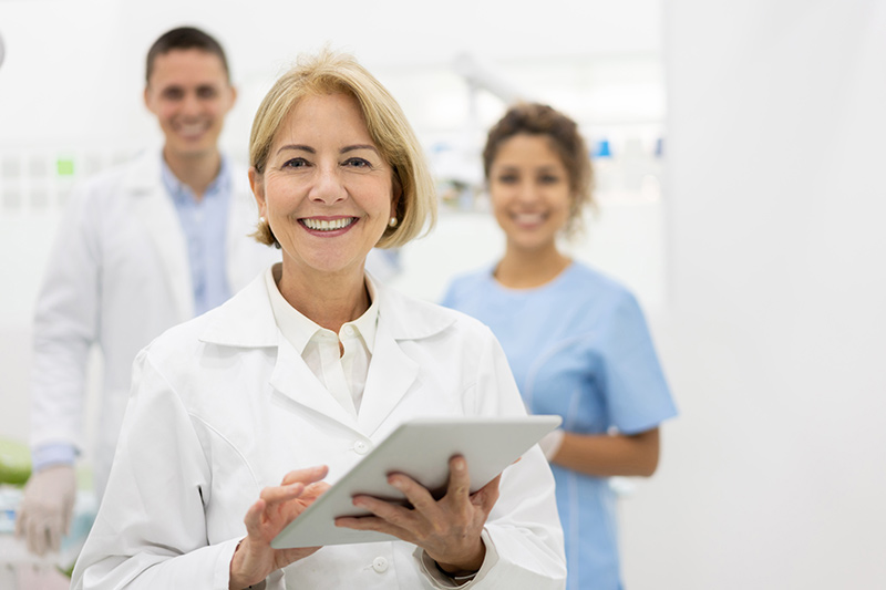 female dentist standing in front of two dental assistants
